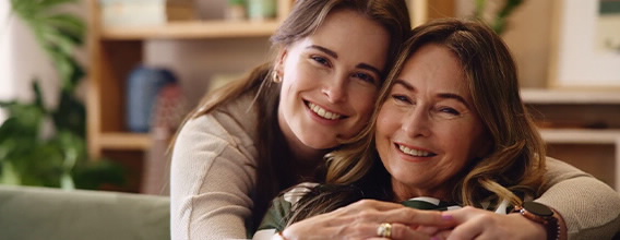 Conheça, ainda vai A Tempo. Duas mulheres, de gerações diferentes, sorridentes e abraçadas num sofá.