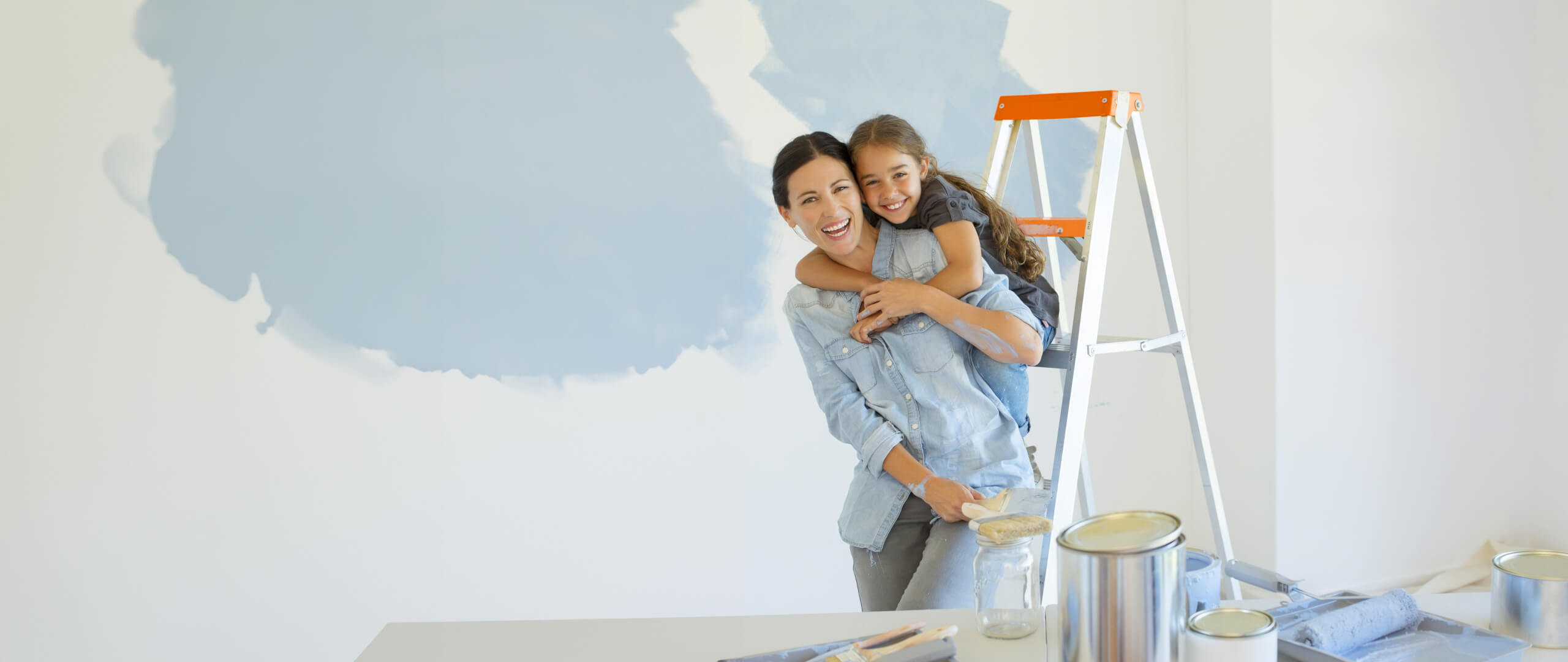 imagem de mãe e filha sorridentes enquanto pintam uma divisão da casa