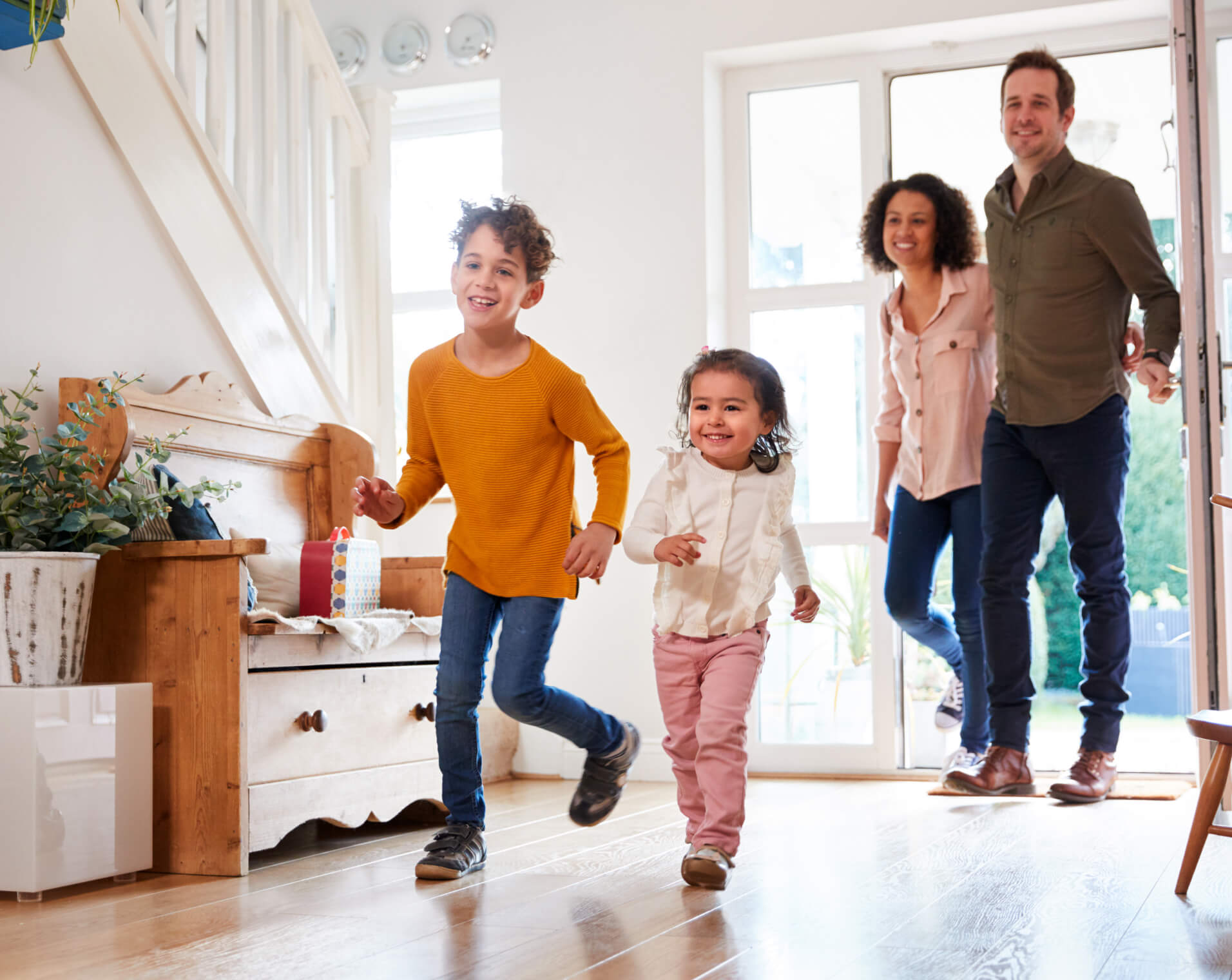 Imagem de família com um casal e duas crianças a entrar em casa sorridente