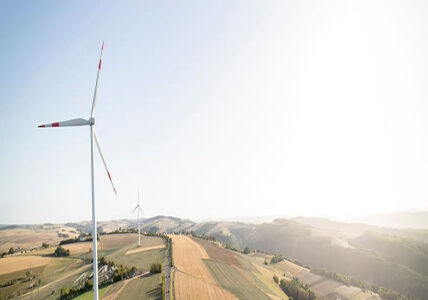 Vista aérea de uma planície verdejante com 2 torres de turbinas eólicas. BPI Impacto Clima Dinâmico.